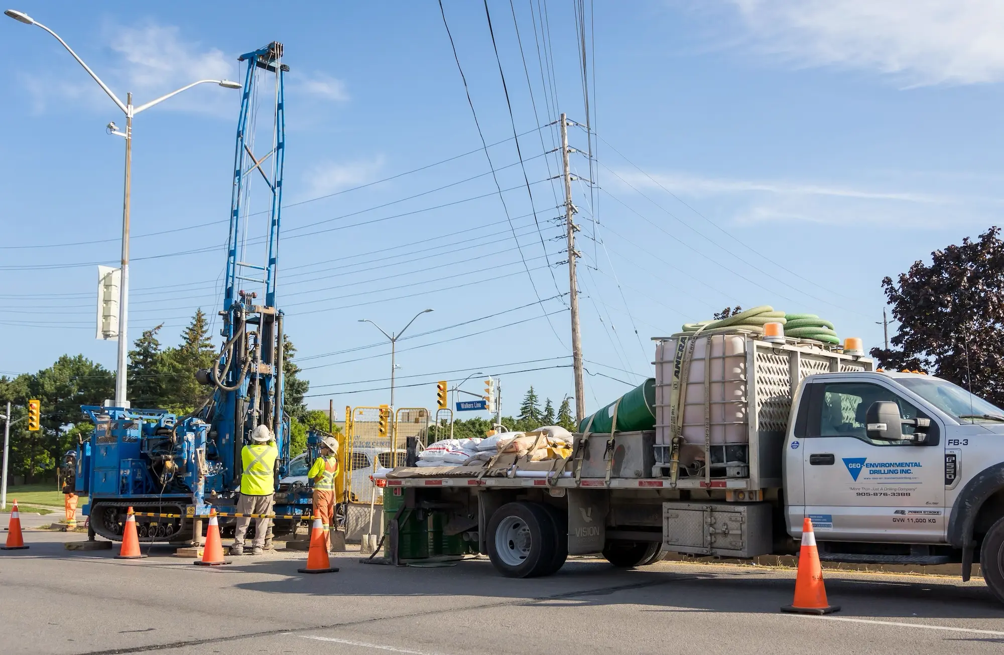 Geo crew operating a track-mounted drill beside a service truck on a city street