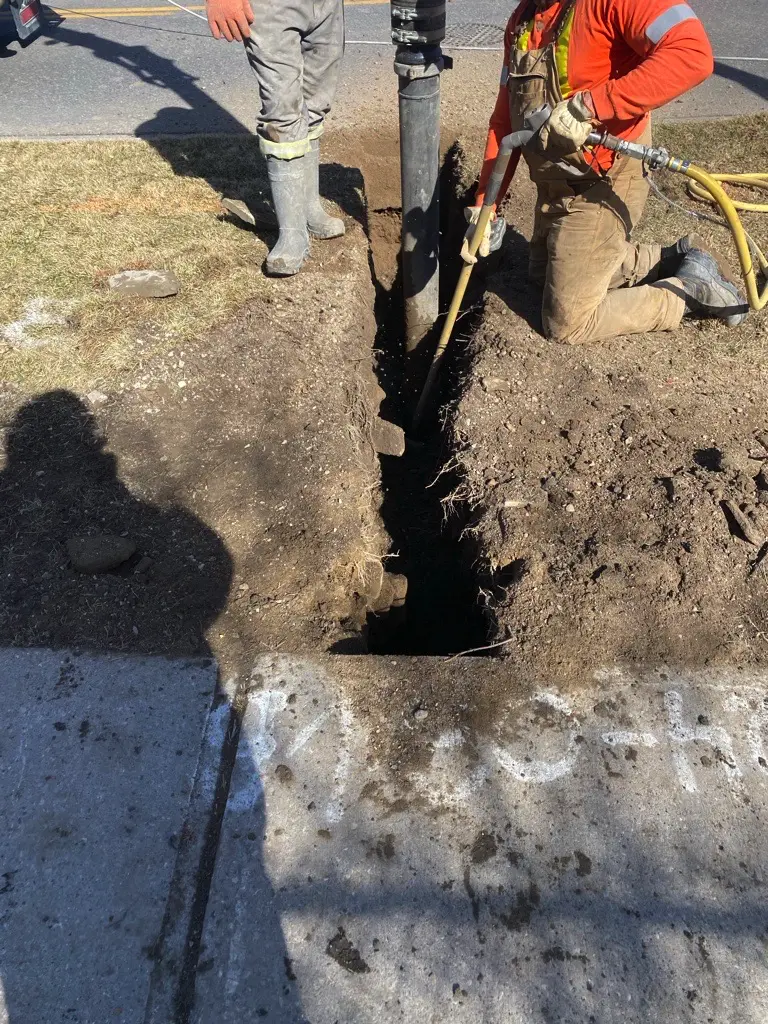 GEO crew member using an air-excavation tool at a marked work point